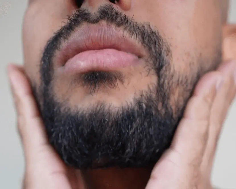 Close-up of a man's face with a beard and mustache, holding his chin.